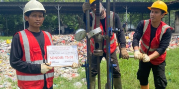 Tiga pekerja teknis Khandaq dengan helm dan rompi keselamatan sedang melakukan uji sondir tanah menggunakan alat mekanis di lokasi proyek Kalideres, memegang papan identifikasi bertuliskan Sondir TS 01.