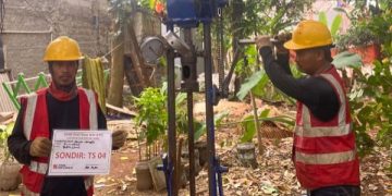 Sebuah deskripsi visual yang terperinci dan berorientasi pada kata kunci untuk aksesibilitas dan SEO: "Sebuah deskripsi visual rinci dua pekerja geoteknik Tim Khandaq sedang mengoperasikan alat uji sondir ringan (Cone Penetration Test/CPT) manual di lokasi proyek Jembatan Krukut, Limo, Depok. Pekerja sebelah kiri memegang papan identifikasi proyek dengan teks jelas 'SONDIR: TS 04' dan logo KHANDAQ. Pekerja sebelah kanan sibuk mengebor dengan alat tersebut. Latar belakang pepohonan hijau di area luar ruangan di Limo di bawah langit mendung."
