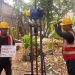Sebuah deskripsi visual yang terperinci dan berorientasi pada kata kunci untuk aksesibilitas dan SEO: "Sebuah deskripsi visual rinci dua pekerja geoteknik Tim Khandaq sedang mengoperasikan alat uji sondir ringan (Cone Penetration Test/CPT) manual di lokasi proyek Jembatan Krukut, Limo, Depok. Pekerja sebelah kiri memegang papan identifikasi proyek dengan teks jelas 'SONDIR: TS 04' dan logo KHANDAQ. Pekerja sebelah kanan sibuk mengebor dengan alat tersebut. Latar belakang pepohonan hijau di area luar ruangan di Limo di bawah langit mendung."